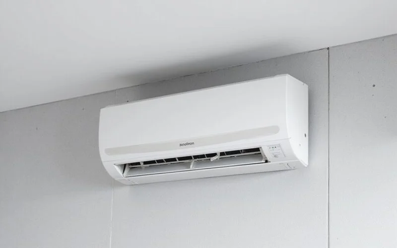 A technician in a blue uniform carefully servicing a wall-mounted split unit air conditioner inside a modern Petaling Jaya apartment, with tools laid out neatly on a cloth below